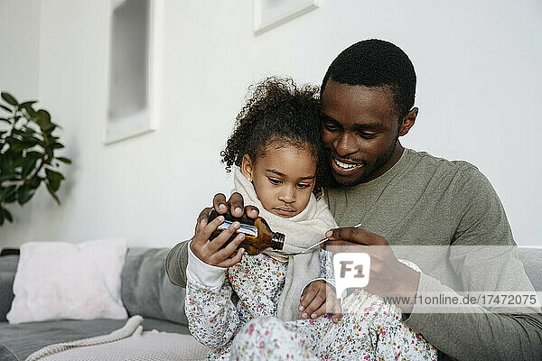 Smiling man giving medicine to daughter on sofa
