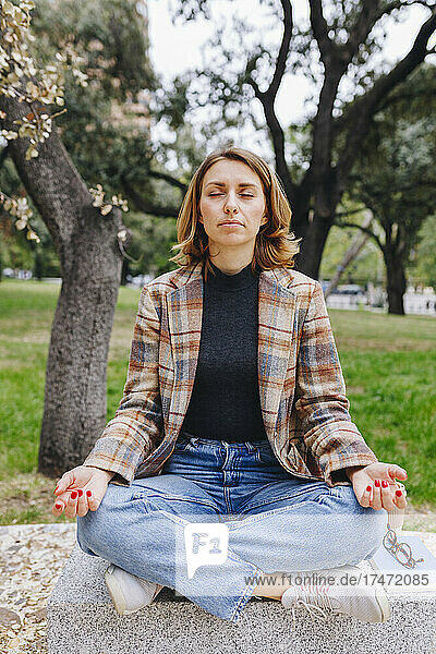Freelancer meditating on bench at public park