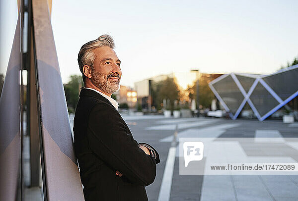 Contemplating businessman with arms crossed leaning on metal