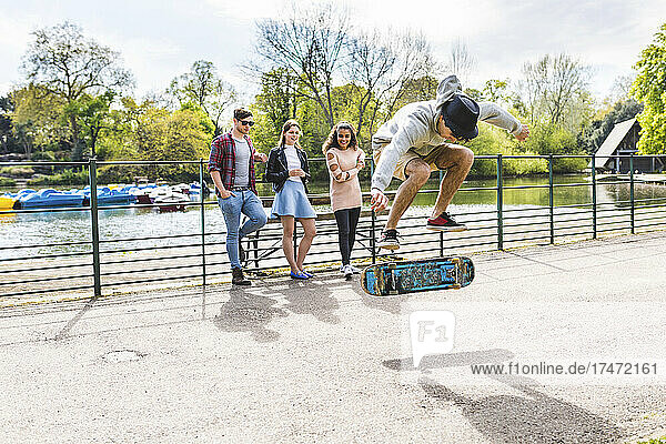 Friends looking at man practicing stunt on skateboard in park