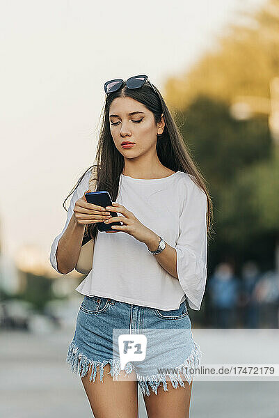 Young woman in denim shorts using smart phone