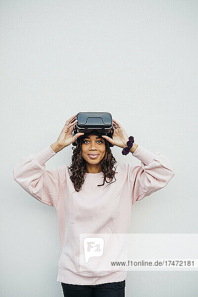 Woman holding virtual reality headset in front of white wall