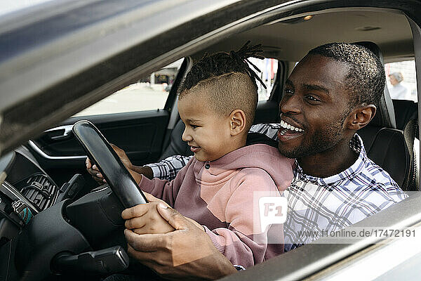 Happy father and son playing with steering wheel in car