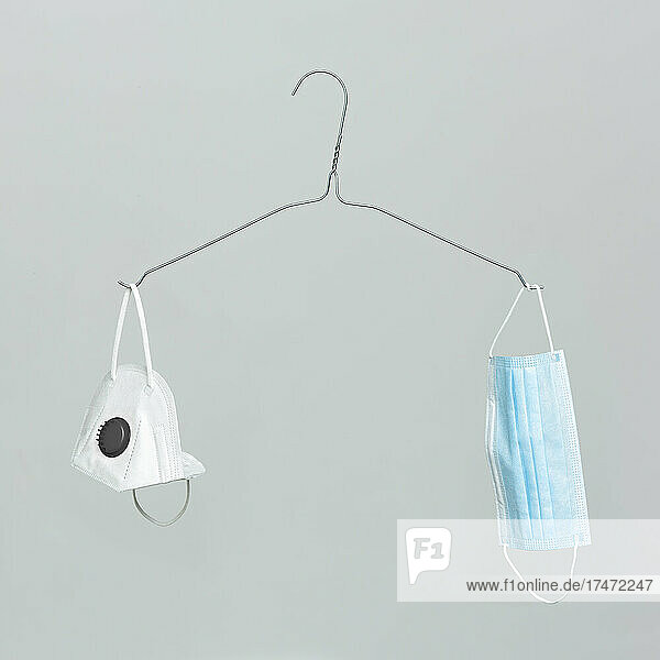 Two protective face masks hanging on coathanger against gray background