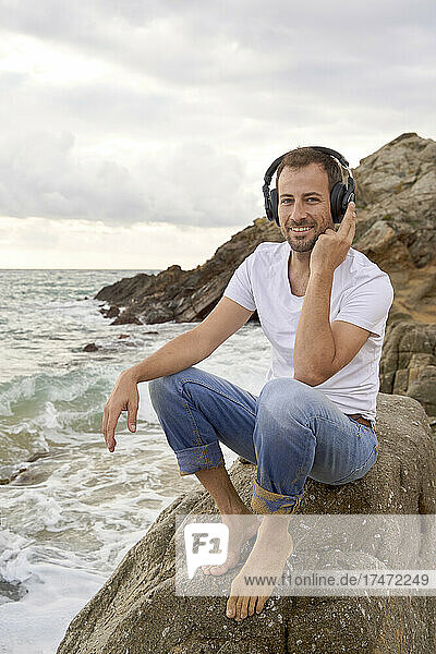 Smiling man listening music on headphones at beach