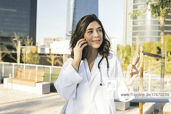 Smiling female doctor talking on smart phone in front of building
