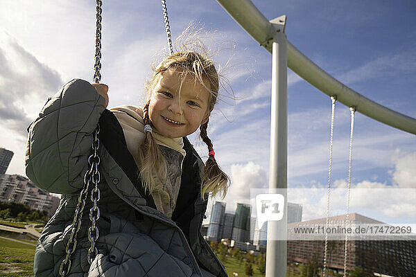 Carefree girl sitting on swing in playground