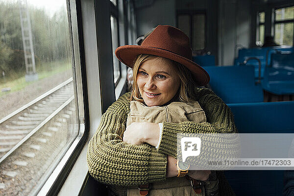 Woman holding backpack while looking through window in train