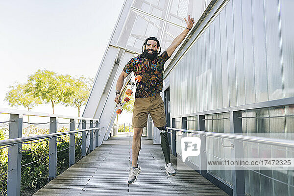 Happy disabled man jumping with skateboard on boardwalk