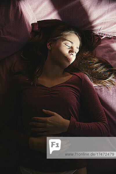 Depressed young woman with eyes closed lying on bed at home