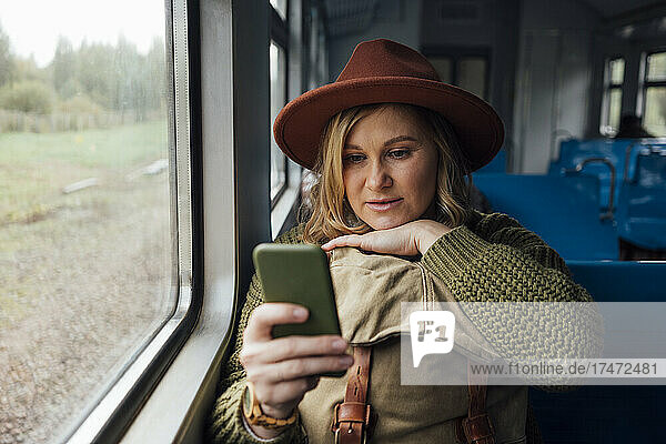 Woman with hat using mobile phone in train