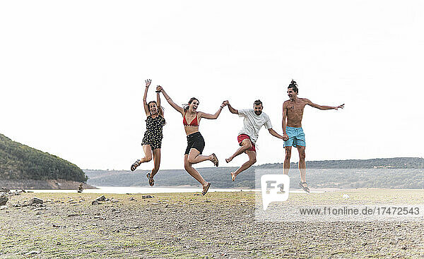 Carefree male and female friends jumping at lakeshore