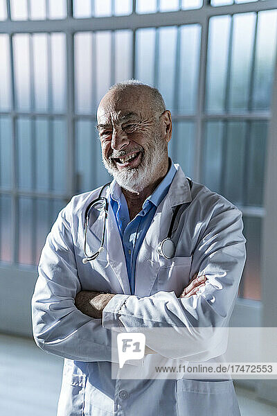 Happy senior doctor in lab coat standing with arms crossed