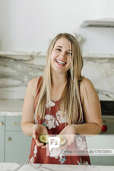 Happy female nutritionist holding avocado in kitchen
