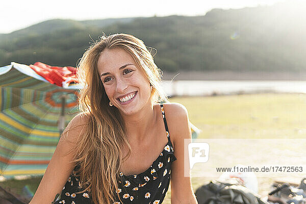 Beautiful young woman smiling at lakeshore during sunny day