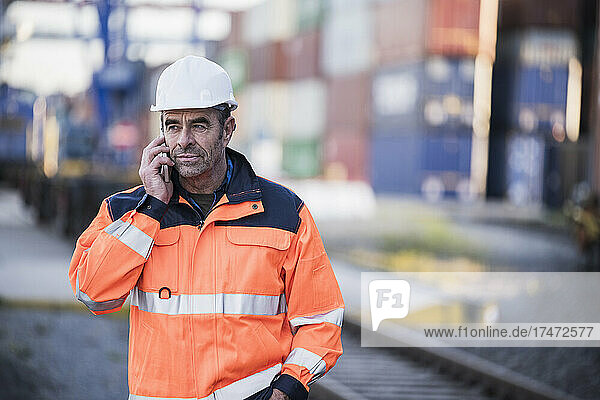 Reifer männlicher Hafenarbeiter  der in der Industrie mit dem Smartphone spricht