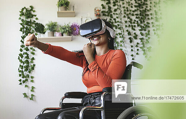 Lächelnde behinderte Frau mit Virtual-Reality-Headset gestikuliert zu Hause