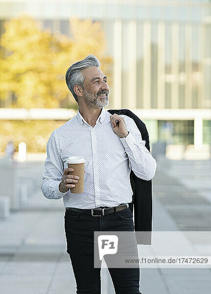 Smiling businessman holding blazer and disposable cup