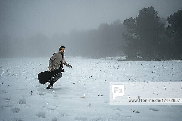 Mature man with guitar case running on snow