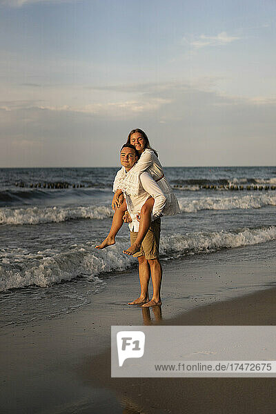 Boyfriend giving girlfriend piggyback ride at beach on sunset