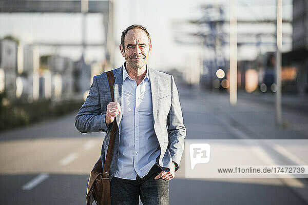 Confident businessman with shoulder bag walking on street