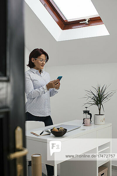 Geschäftsfrau schreibt Textnachrichten auf dem Smartphone  während sie im Heimbüro steht