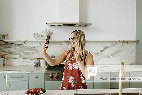 Female nutrient expert waving hand during video call through smart phone in kitchen