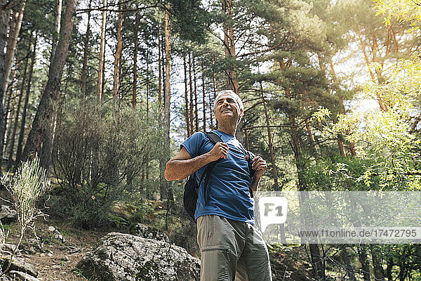 Smiling male tourist with backpack standing in forest during vacation