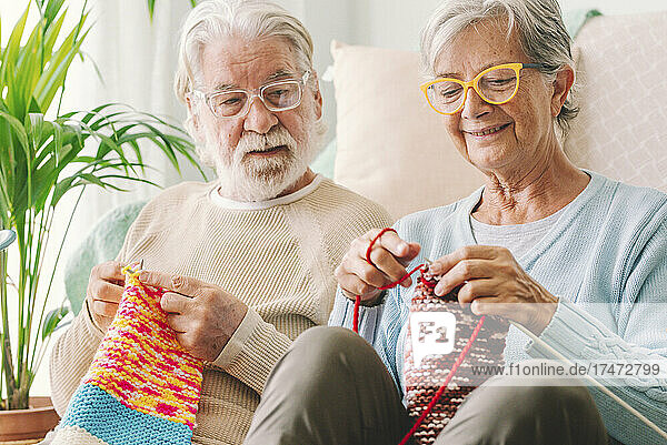 Senior man looking at woman knitting wool at home