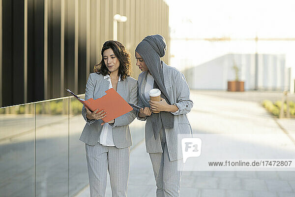 Young businesswoman discussing with female colleague over file on footpath