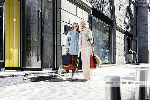 Happy women with shopping bags standing near store