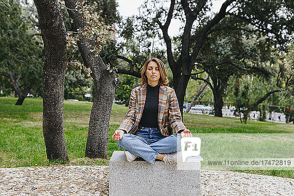 Businesswoman meditating on bench at public park