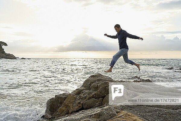 Playful man jumping over rocks near sea at beach