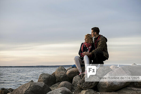 Couple looking at sea while sitting on rock