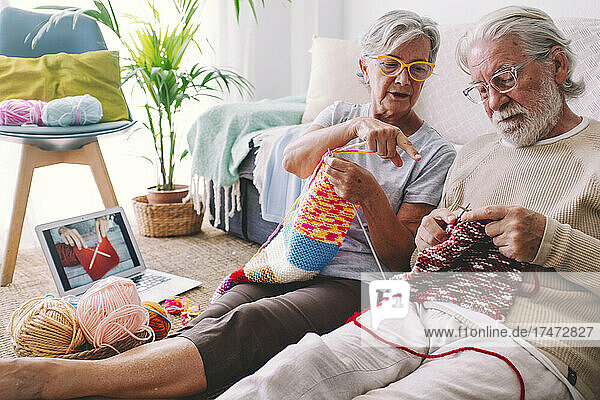 Woman teaching man to knit wool with needle at home