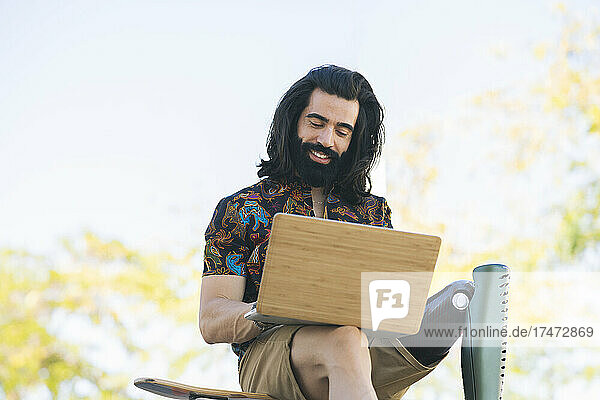 Smiling disabled man with long hair using laptop in public park