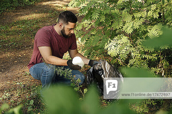 Male activist putting plastic bottle in garbage bag