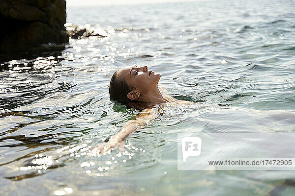 Junge Frau mit geschlossenen Augen schwimmt im Meer
