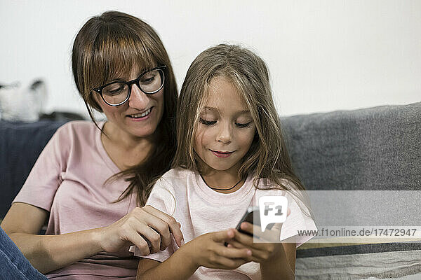 Girl using smart phone with woman at home