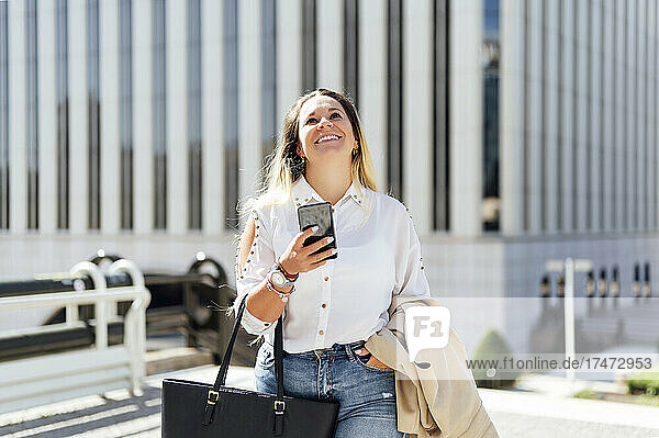 Happy businesswoman with smart phone looking up