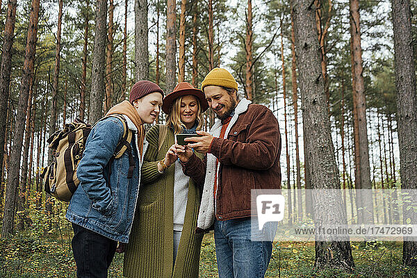 Family sharing smart phone while standing in forest