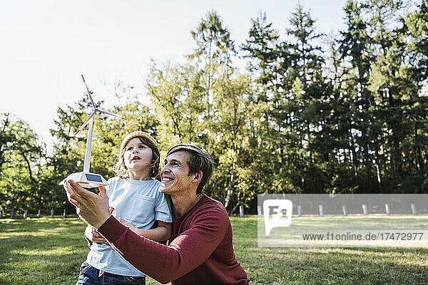 Father holding wind turbine model with son at park
