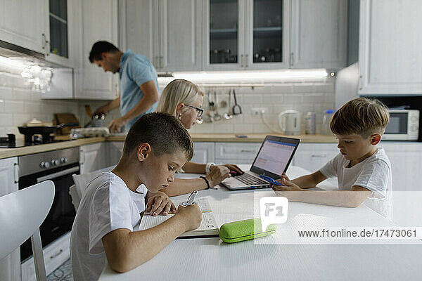 Junge lernt zu Hause am Tisch mit der Familie im Hintergrund