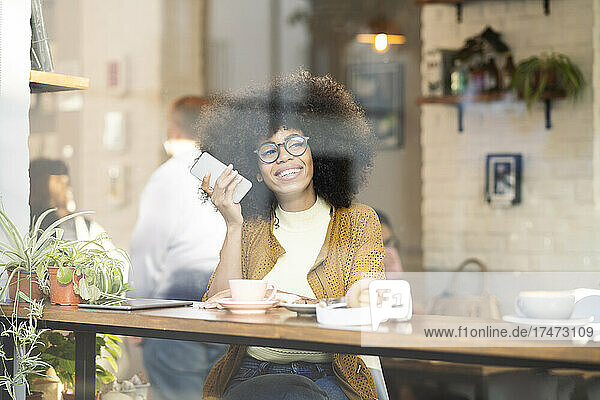 Lächelnde Frau  die im Café ihr Mobiltelefon hört