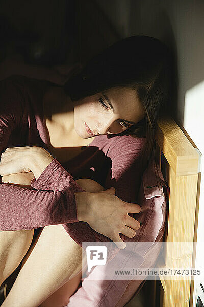 Lonely young woman sitting on bed in bedroom