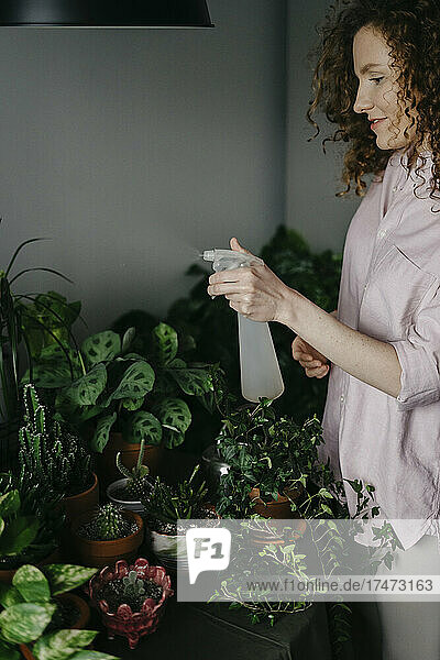 Woman spraying water on plants at home