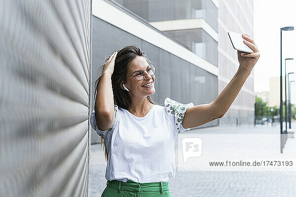 Smiling female professional with hand in hair taking selfie through smart phone