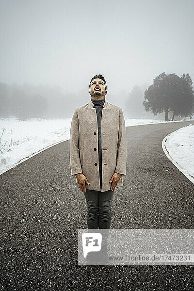 Mature man looking up while standing on road during winter