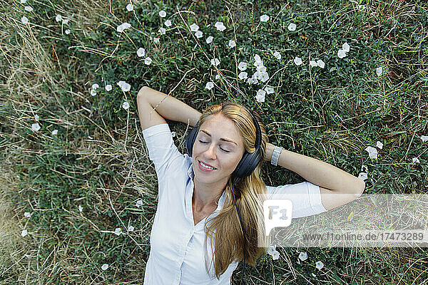 Beautiful woman with wireless headphones relaxing on grass