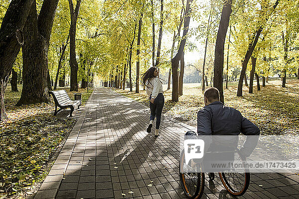 Girlfriend running with disabled boyfriend moving in wheelchair at park